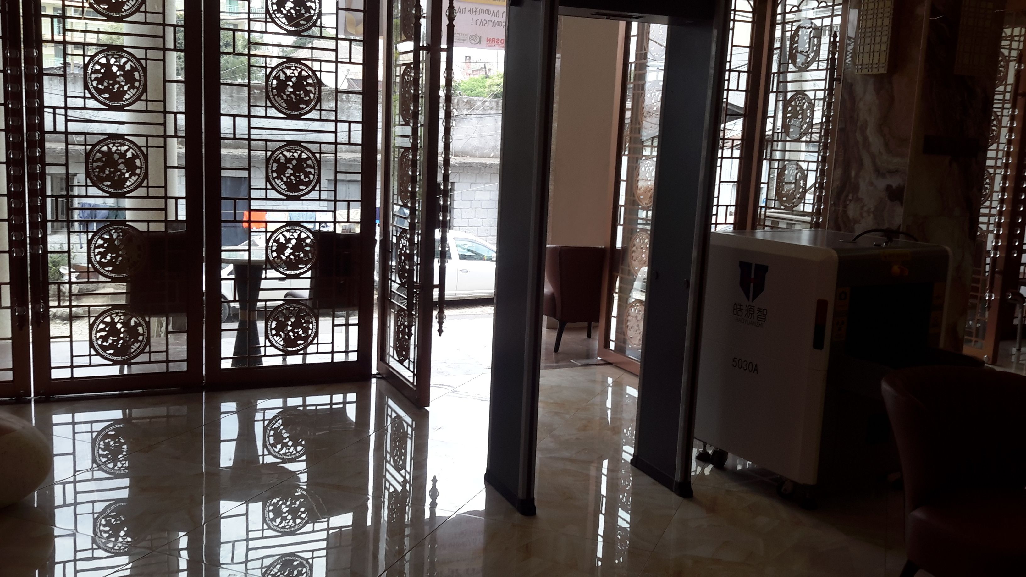 A hotel room with a large window, a chair, a small table, and a refrigerator.