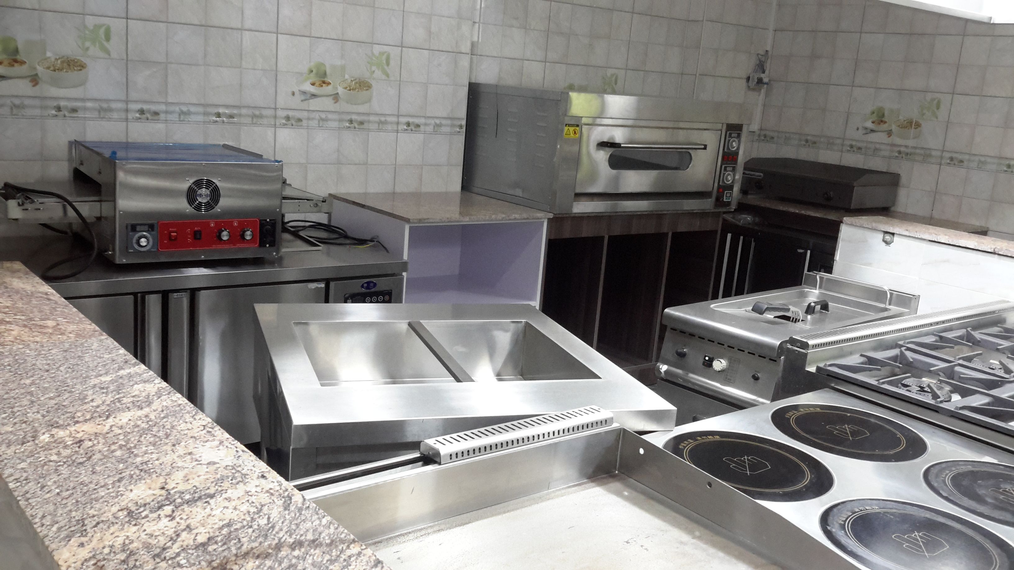 Ammattikäyttöön tarkoitettu keittiö, jossa on ruostumattomasta teräksestä valmistettuja laitteita, kuten monitoimikone, uppopaistinpannu ja liesi, jossa on useita keittolevyjä.
