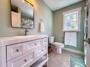 A bathroom with a white vanity, a toilet, and a window with a view of trees.