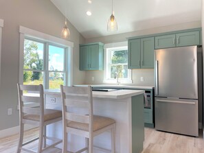 A kitchen with teal cabinets, a stainless steel refrigerator, and a bar area with two wooden chairs.