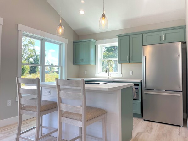 A kitchen with teal cabinets, a stainless steel refrigerator, and a bar area with two wooden chairs.