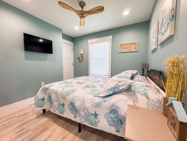 A bedroom with a bed, a ceiling fan, a TV, and artwork on the walls.