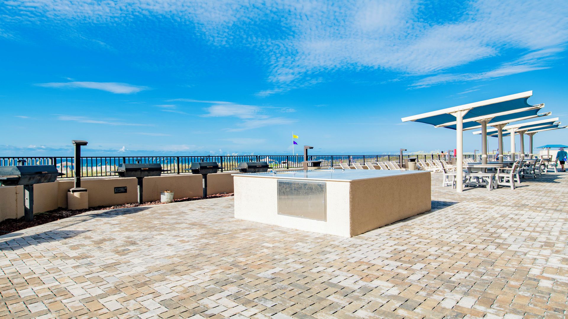 Un patio frente a la playa con zona de barbacoa, mobiliario y vista al océano.