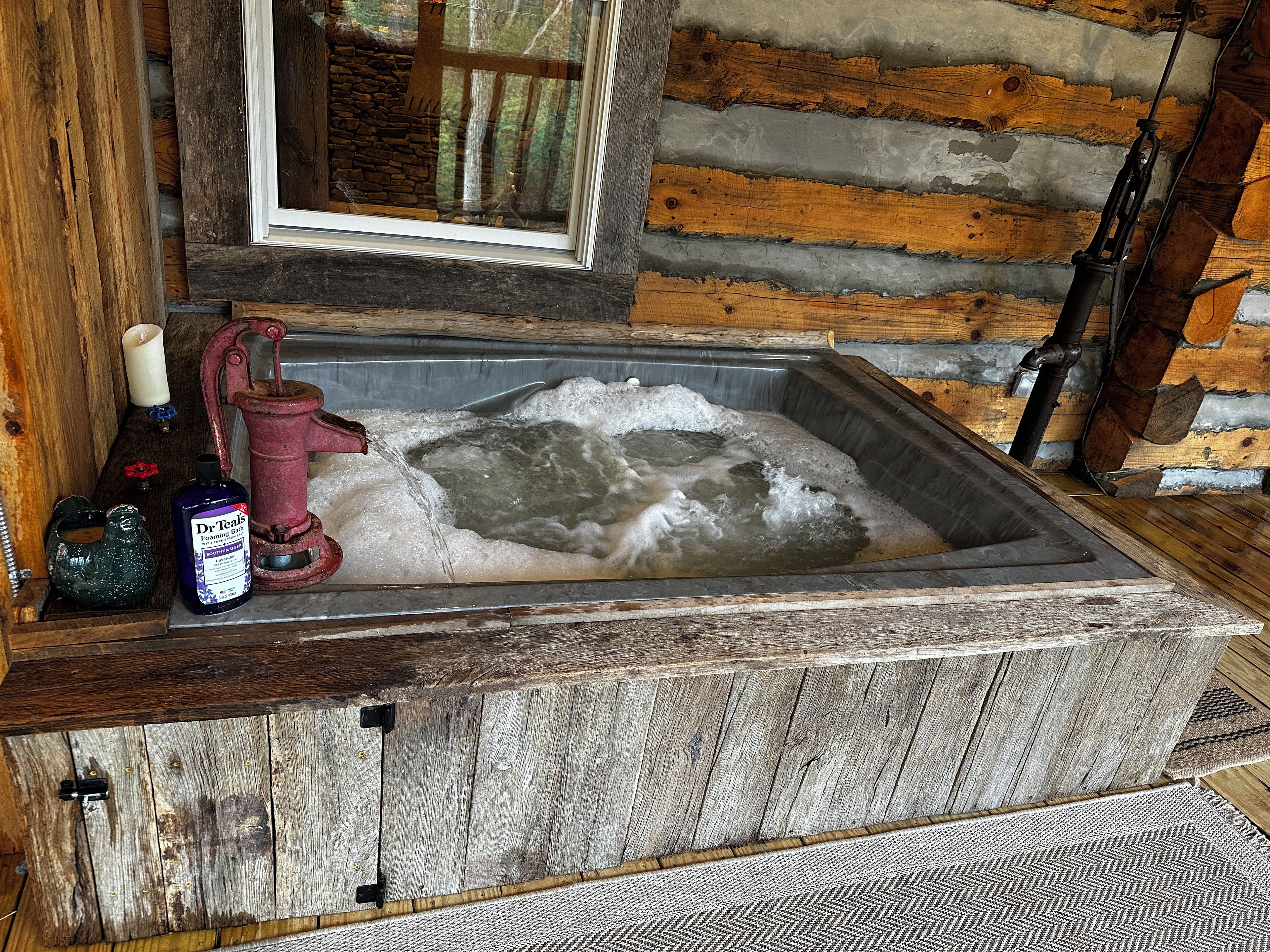A rustic wooden cabin with a stone fireplace, a wooden bench, and a window with a view of trees.