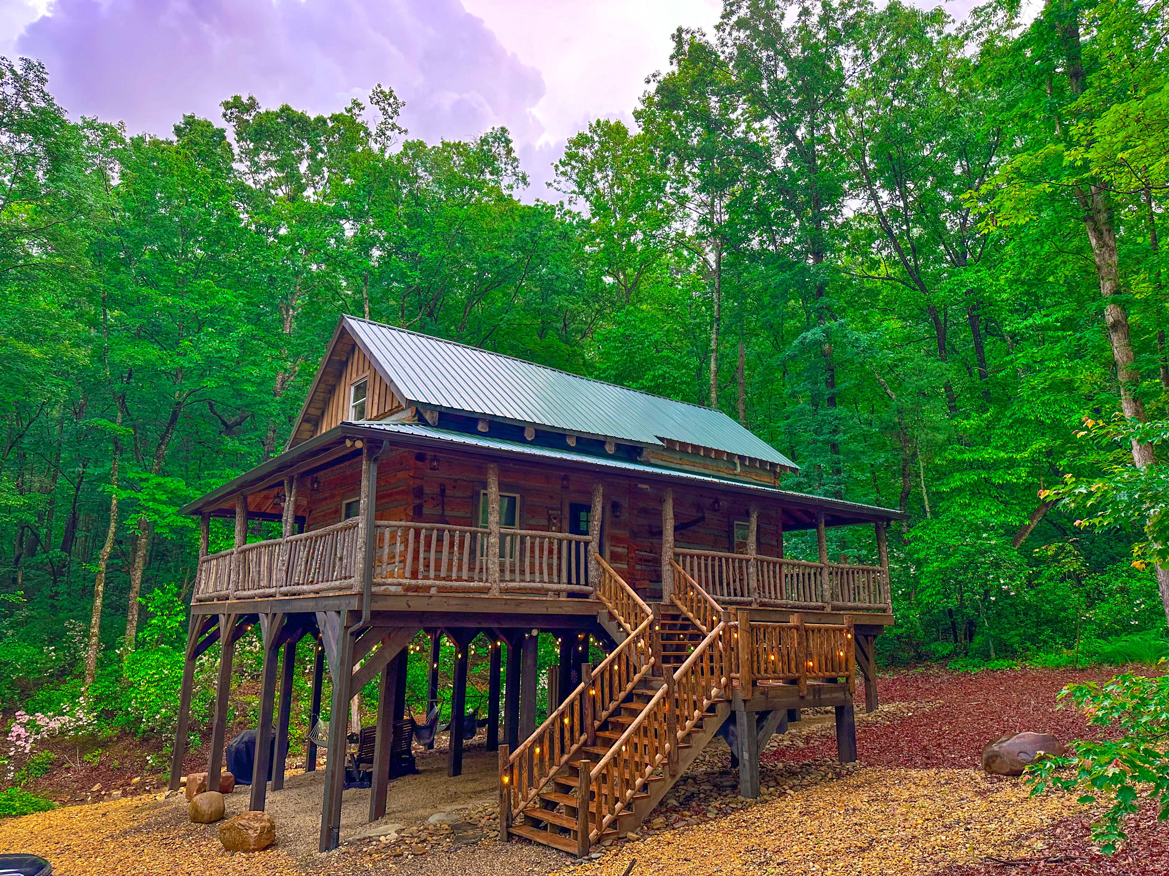 A wooden cabin with a balcony and a staircase, surrounded by dense forest.