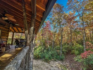 A rustic cabin with a wooden deck, a dining area, and a view of a forest with autumn foliage. - Treehouse cabin Cozy 2-bedroom in Dobson, NC (Dobson)