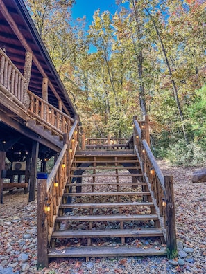 Un escalier en bois mène à une zone abritée, délimitée par une balustrade, et est entouré d’un feuillage automnal.
