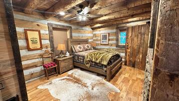 A log cabin-style bedroom with a bed, a wooden nightstand, a lamp, a framed picture, and a ceiling fan.