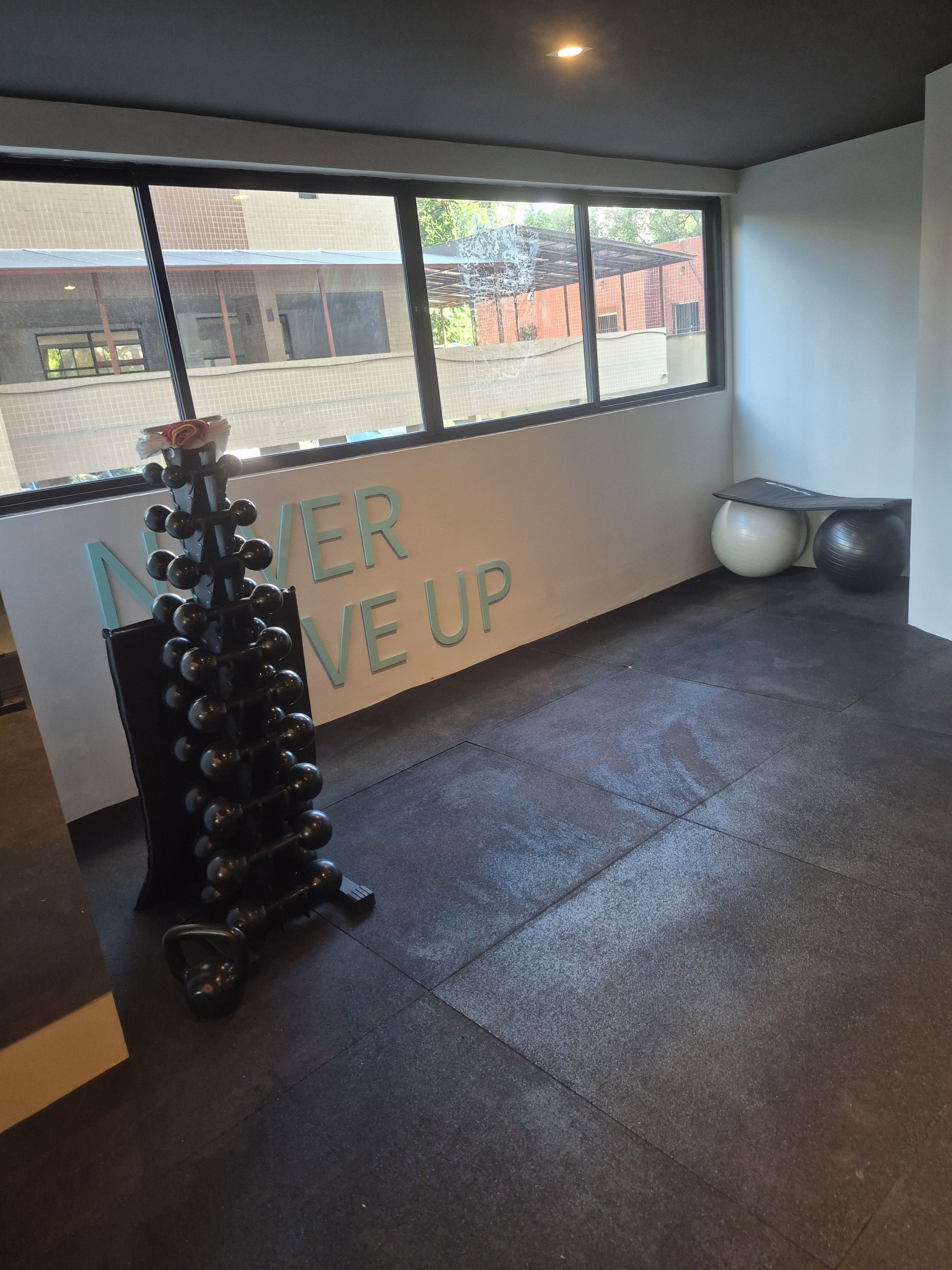 Ett gym med en träningsmaskin som är monterad på väggen, ett stort fönster och en motiverande skylt.