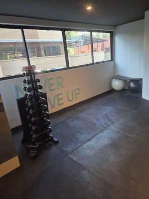 Ein Fitnessraum mit an der Wand befestigtem Trainingsgerät, einem großen Fenster und einem motivierenden Spruch.