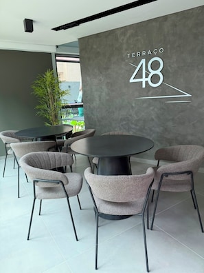 Ein modernes Interieur mit einem runden Tisch, sechs Stühlen, einer strukturierten Wand in Grau und dem Schriftzug 'TERRACAO 48'.