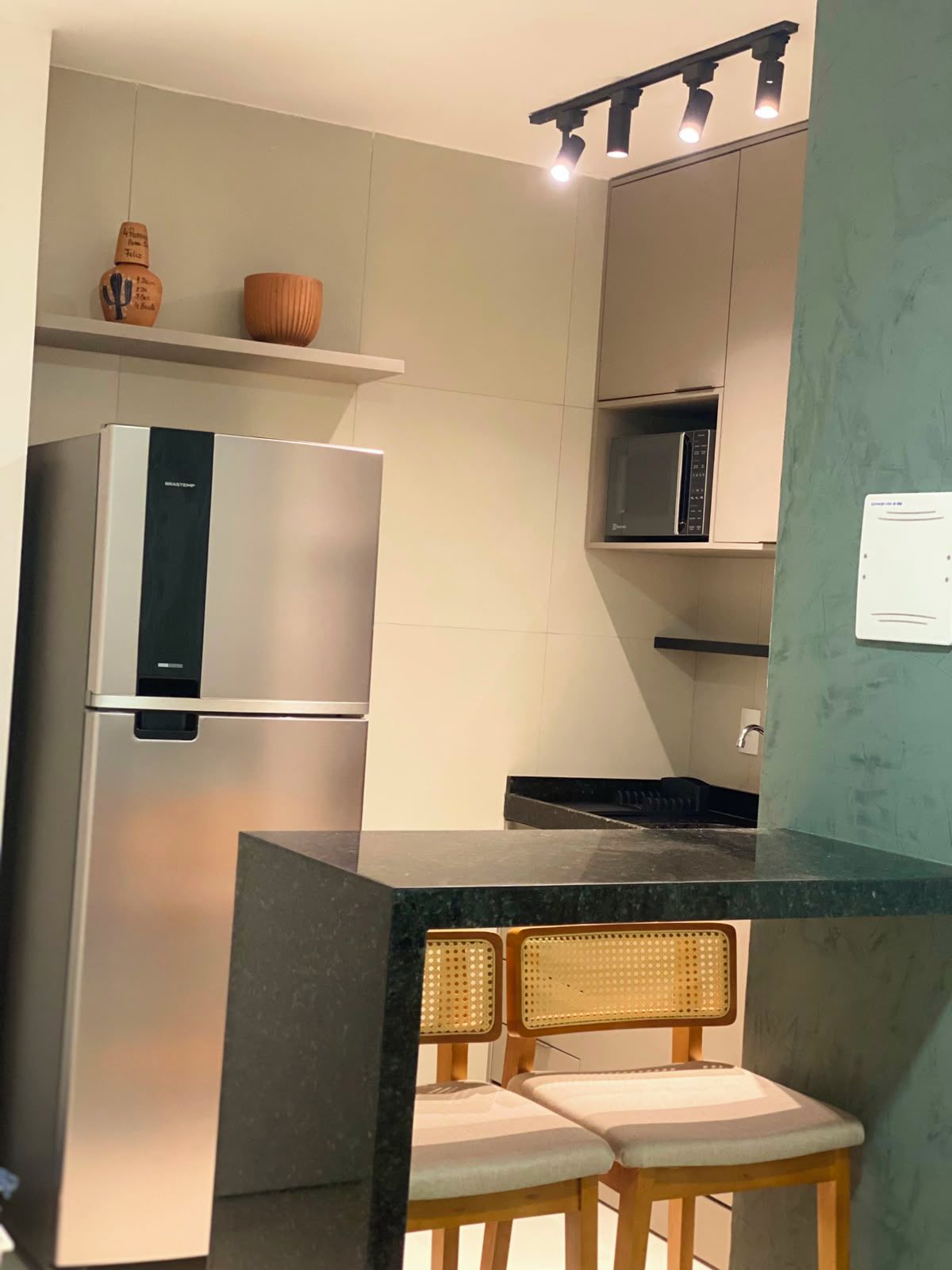 A modern kitchen with a stainless steel refrigerator, a microwave, and a bar area with two wicker chairs.