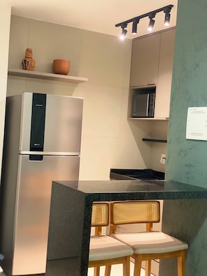 A modern kitchen with a stainless steel refrigerator, a microwave, and a bar area with two wicker chairs. - New Listing (Recife)