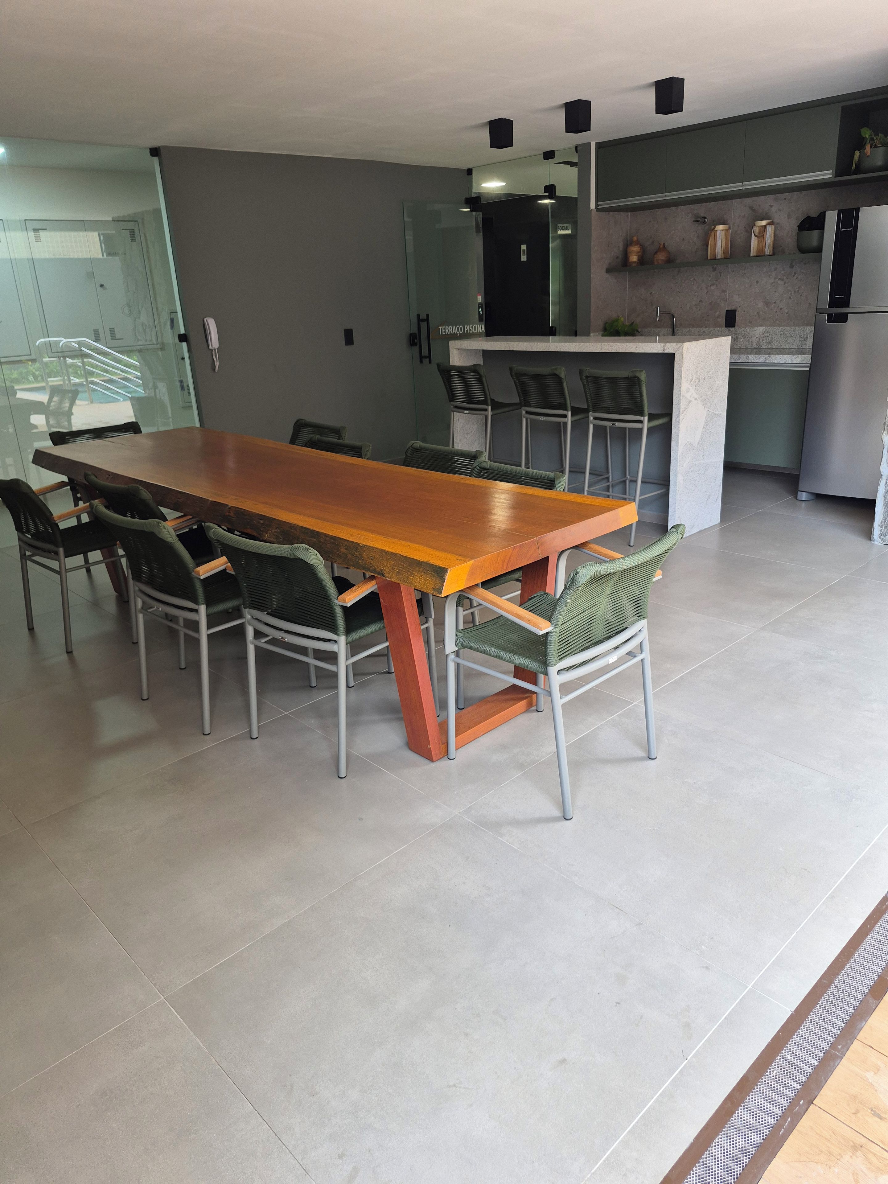 A modern kitchen with a long wooden table and chairs, a built-in bar, and a refrigerator.