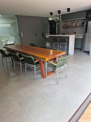 A modern kitchen with a long wooden table and chairs, a built-in bar, and a refrigerator. - New Listing (Recife)