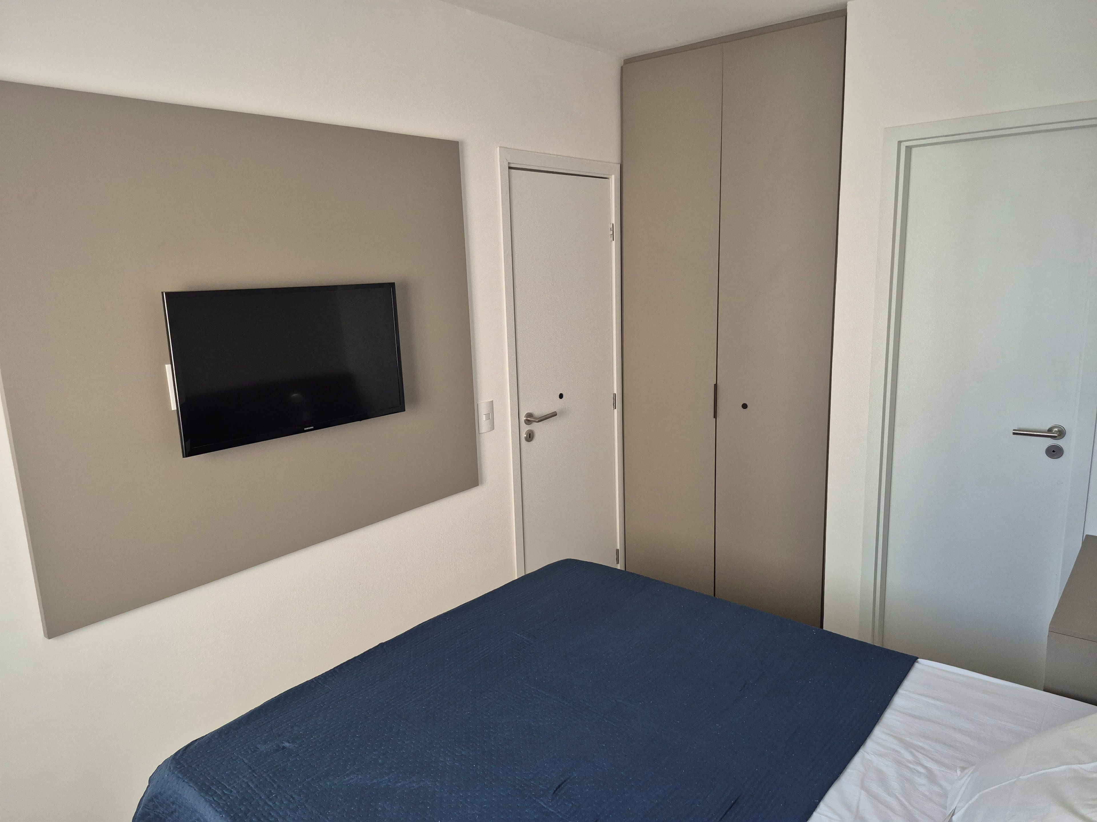 A bedroom with a bed, a television mounted on the wall, and two doors.