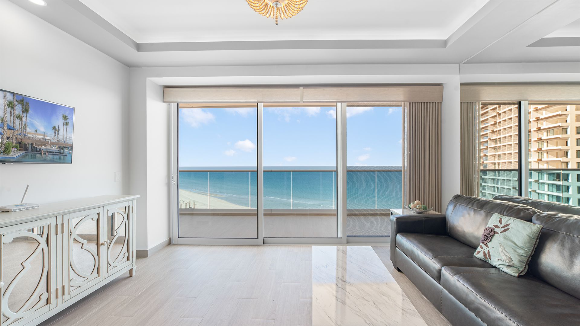 Een ruime woonkamer met een grote schuifpui die uitkomt op een balkon met uitzicht op de oceaan.