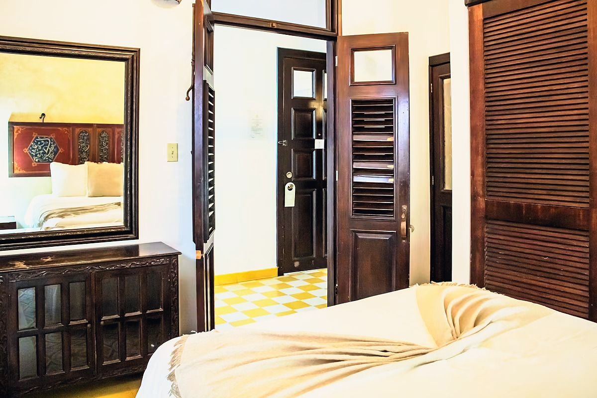 A hotel room with a bed, a dresser, a mirror, and a door leading to another room.