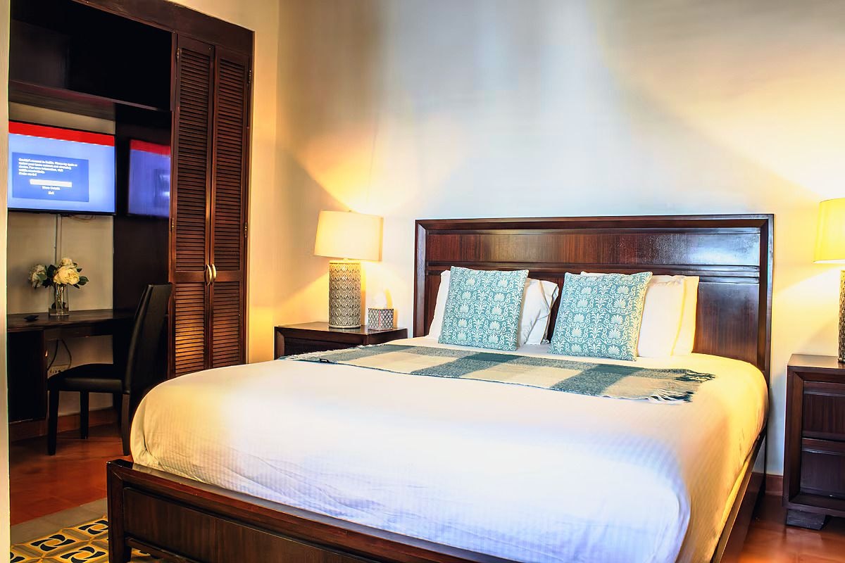 A hotel room with a large bed, two bedside tables, a desk with a chair, and a television on the wall.