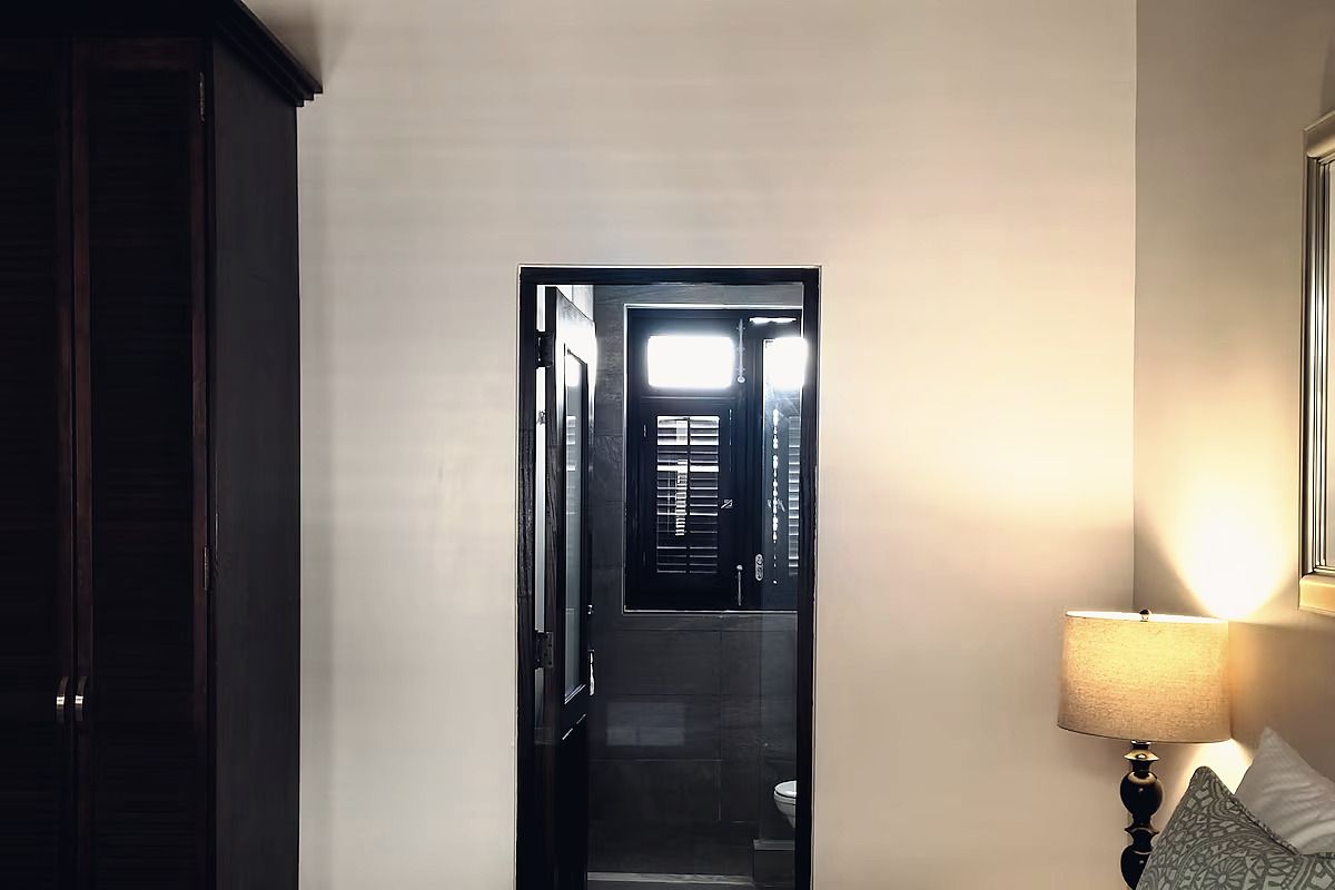A hallway with a door leading to a bathroom, a bedside lamp, and a wall-mounted mirror.
