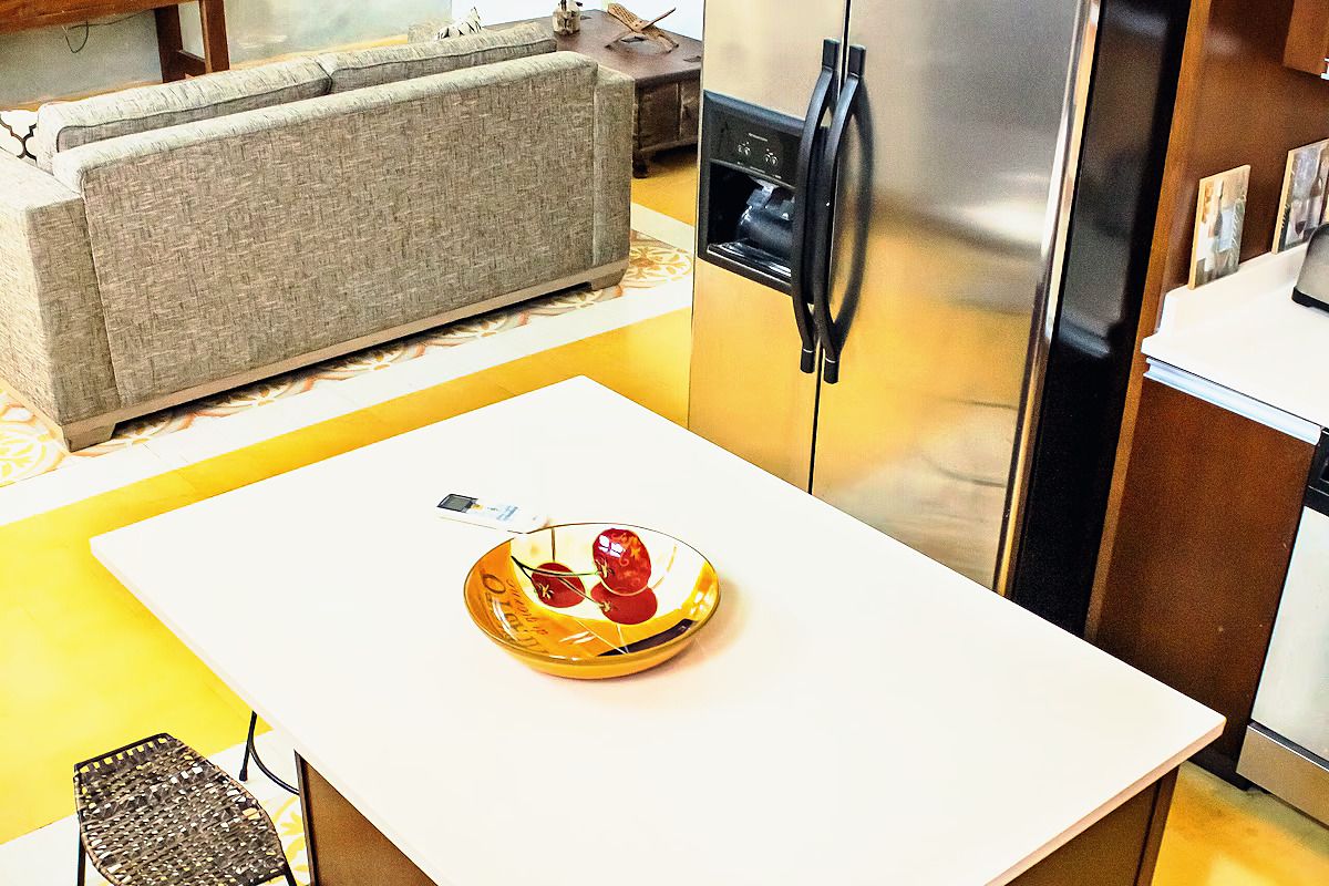 Een keuken met een wit aanrecht, een roestvrijstalen koelkast en een grijze bank.
