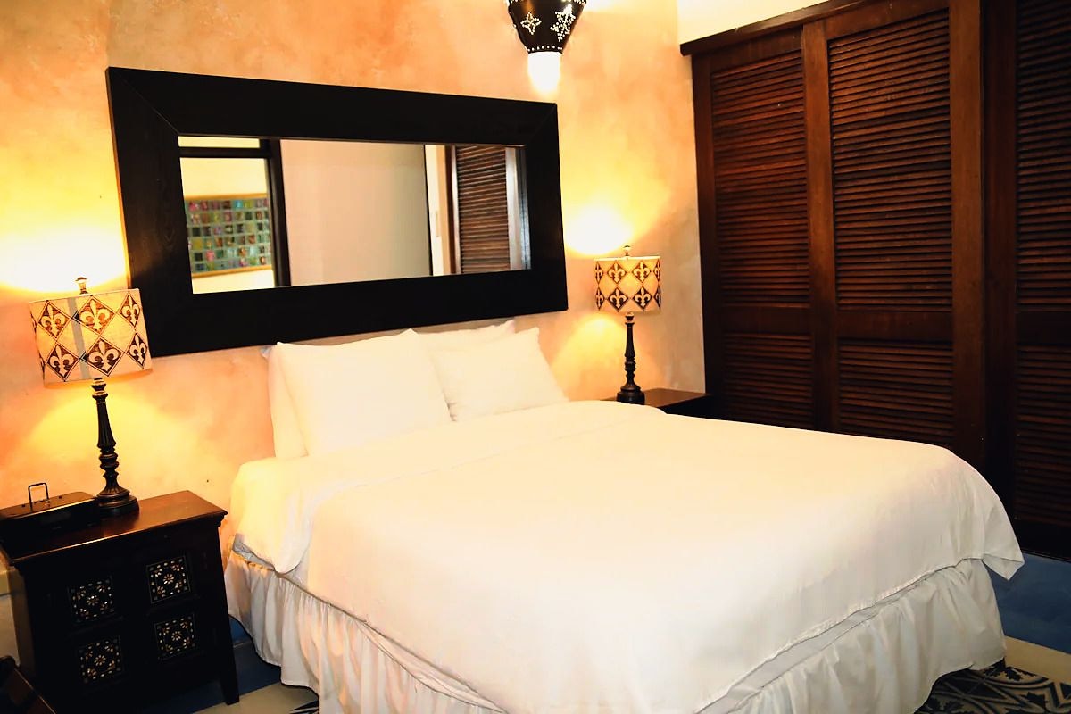 A hotel room with a large bed, two bedside lamps, a mirror above the bed, and a wooden wardrobe.