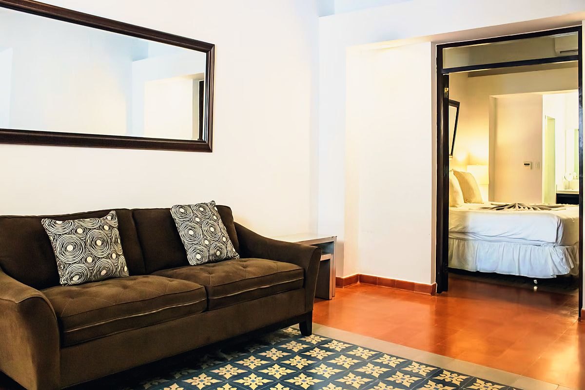 A room with a brown sofa, patterned cushions, a mirror, and a patterned rug.