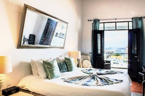 A hotel room with a bed, a large window with curtains, a view of buildings, and a mirror on the wall. - Patio Elba Old San Juan (San Juan)