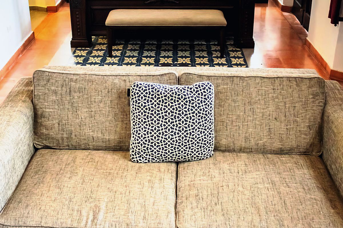A sofa with a patterned pillow in a room with patterned flooring and a bench in the background.