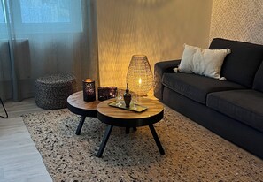 A modern living room with a dark sofa, two round tables with candles, and a textured rug. - New Listing (Royan)