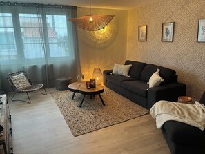 Ett modernt vardagsrum med en soffa, en fåtölj, ett soffbord och en hängande lampa.