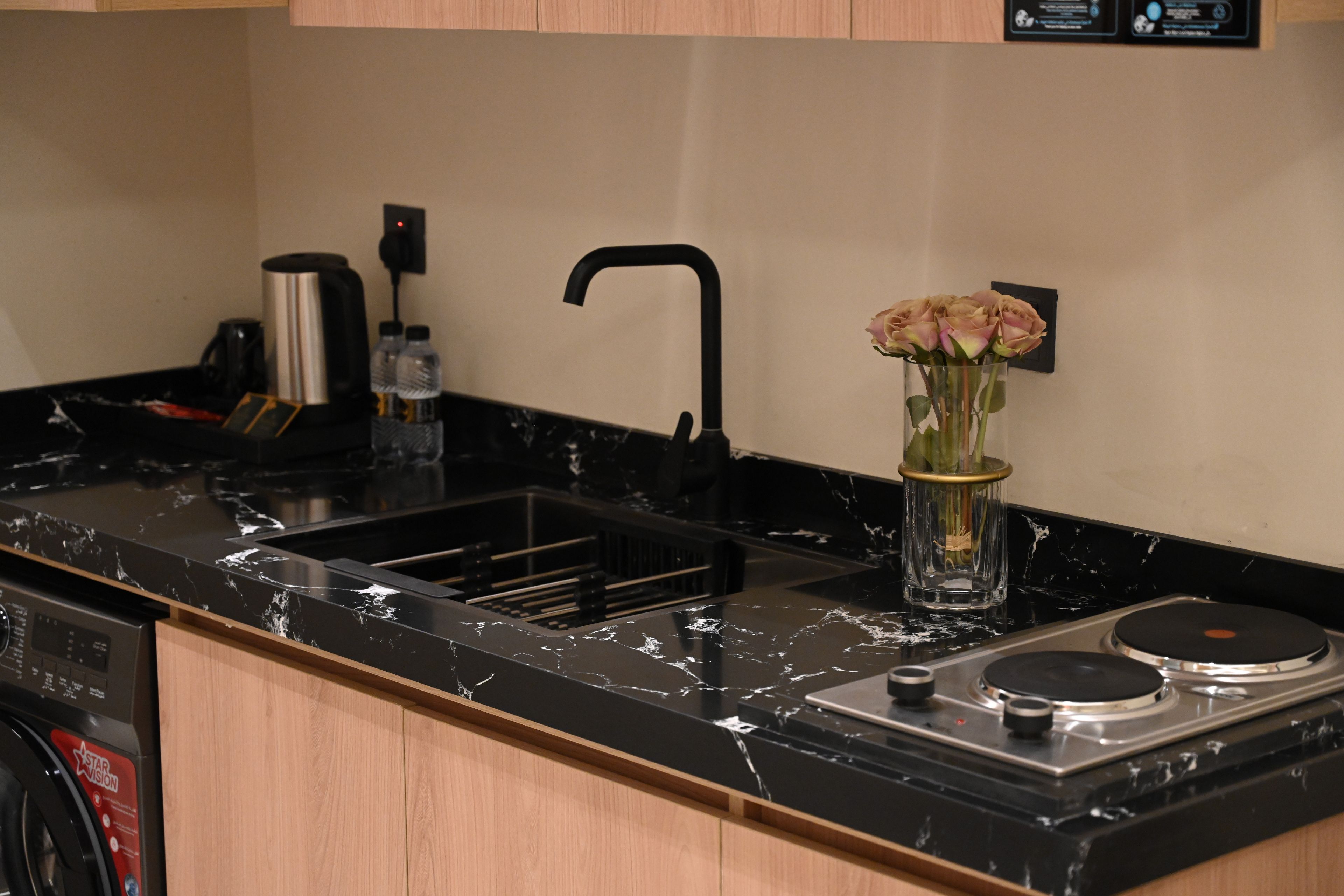 A kitchen with a black marble countertop, a stainless steel sink, a coffee maker, and a vase with flowers.
