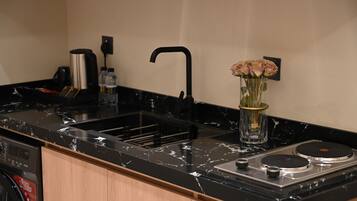 A kitchen with a black marble countertop, a stainless steel sink, a coffee maker, and a vase with flowers.