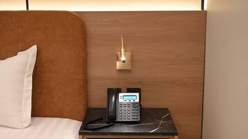 A hotel room with a wooden headboard, a bedside table with a black telephone, and a wall-mounted light fixture.