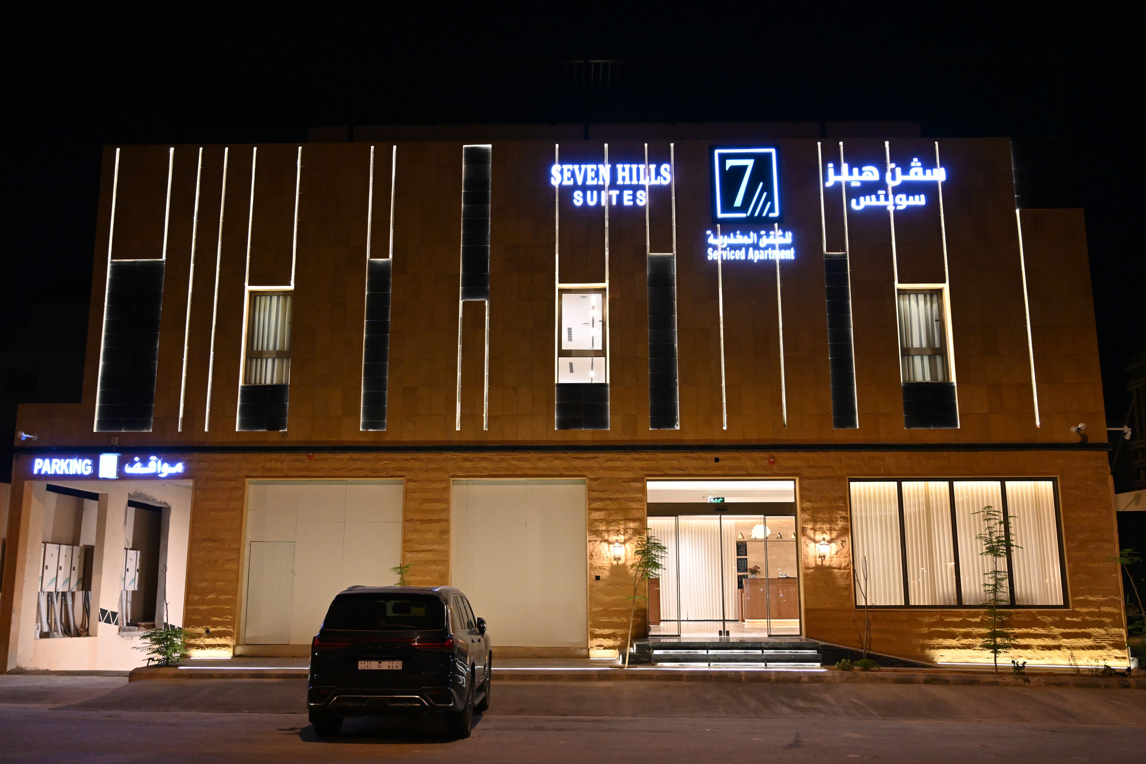 Un hotel con fachada moderna, varios accesos y una zona de estacionamiento.