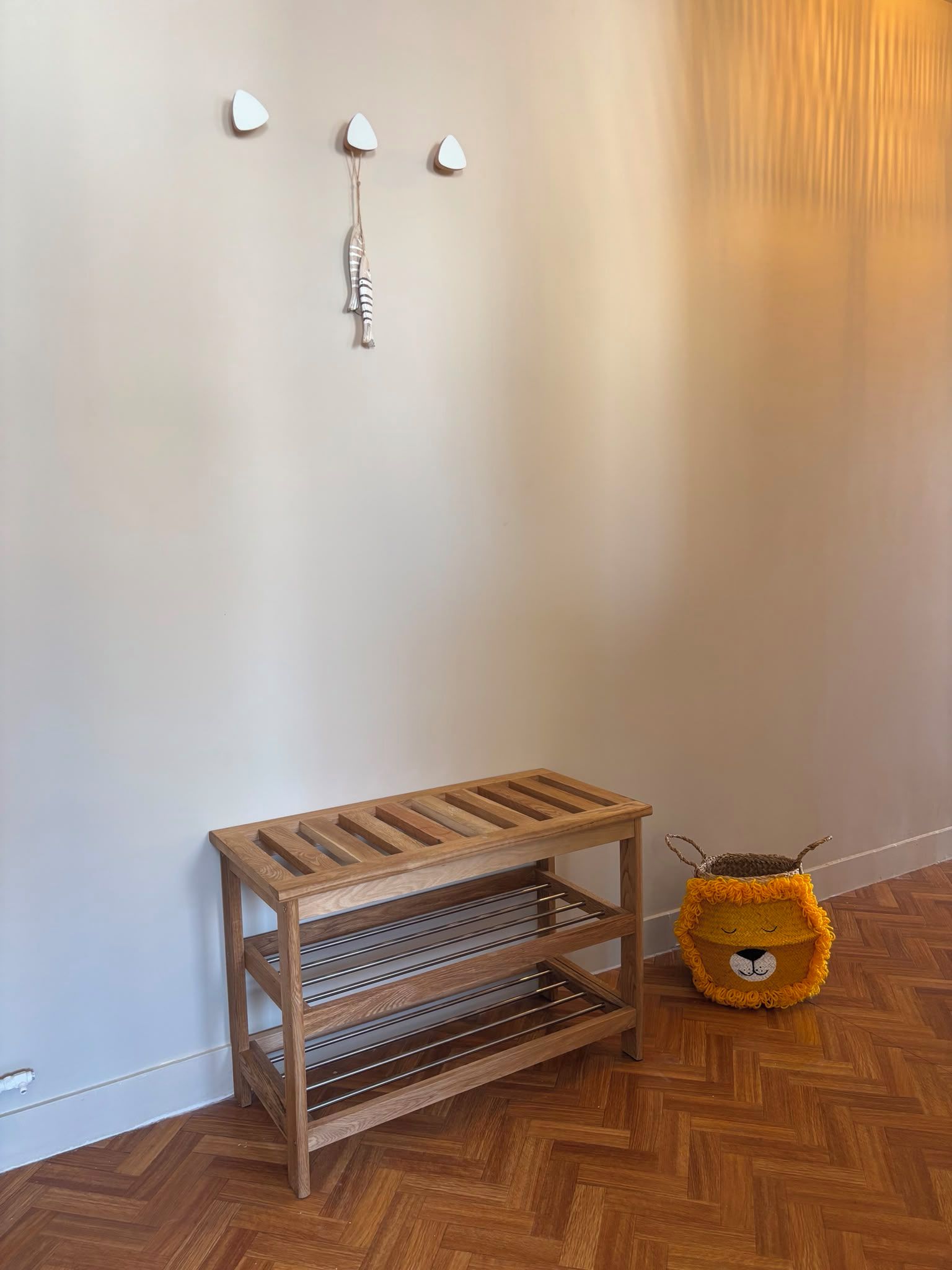 Un banc en bois avec des étagères en métal adossé à un mur, un petit objet décoratif suspendu au-dessus, et un jouet en peluche posé sur le sol.