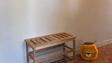 Un banc en bois avec des étagères en métal adossé à un mur, un petit objet décoratif suspendu au-dessus, et un jouet en peluche posé sur le sol.