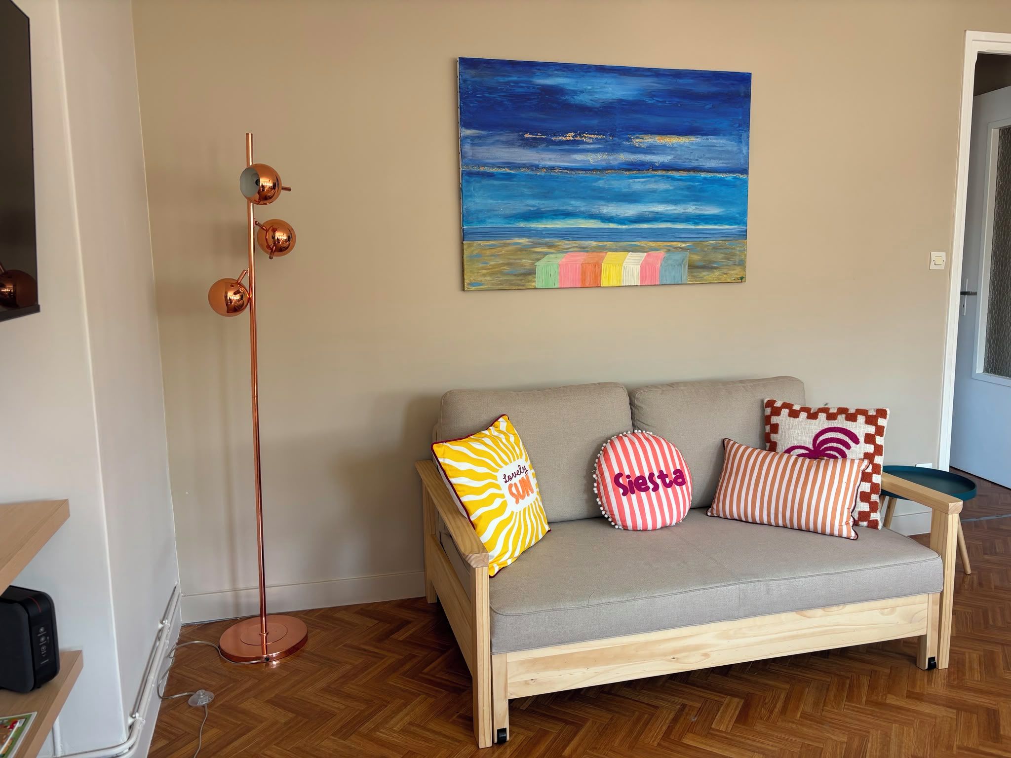 Un salon avec un canapé, des coussins colorés, un grand lampadaire et un tableau accroché au mur.