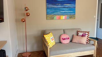 Un salon avec un canapé, des coussins colorés, un grand lampadaire et un tableau accroché au mur.
