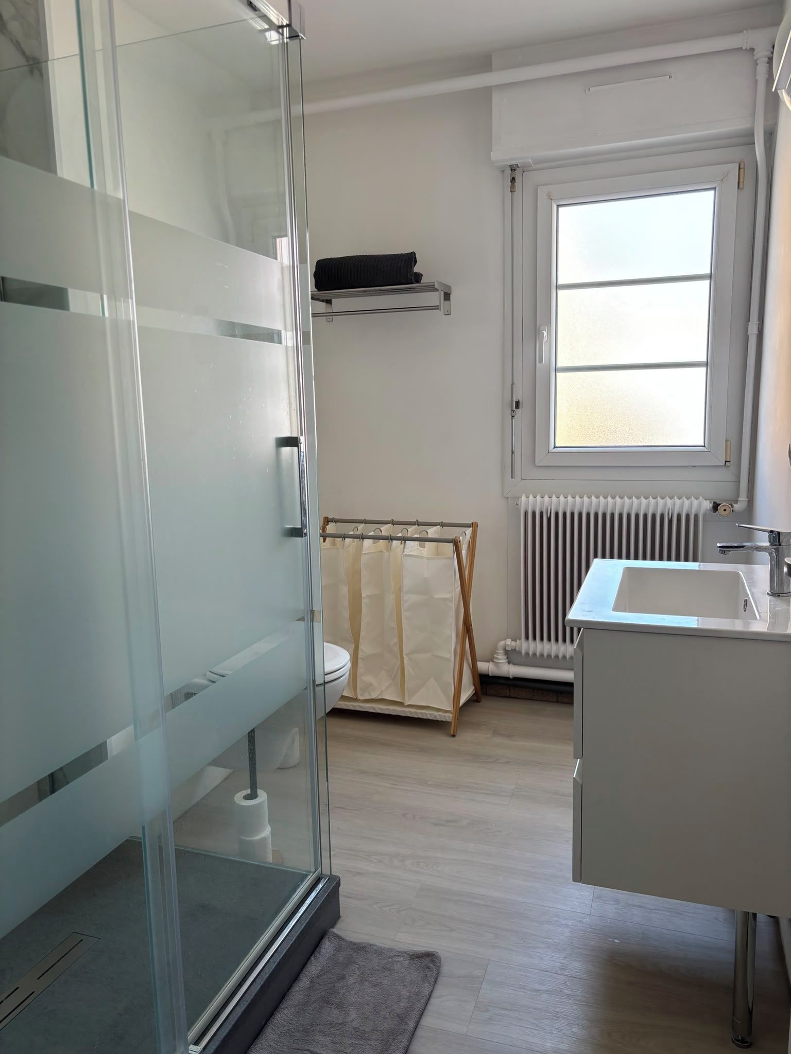 Une salle de bain moderne avec une douche à parois de verre, un lavabo blanc et une fenêtre laissant entrer la lumière naturelle.