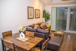 A modern living room with a sofa, a dining table, and a small coffee table. - 3-Bed House Sleeps 7 with Parking · Garden · Walk to Peel Park, Salford (Greater Manchester)