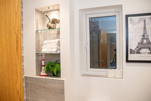 Un bagno con uno scaffale in vetro che contiene asciugamani, una decorazione a forma di faro e una finestra con carta igienica.