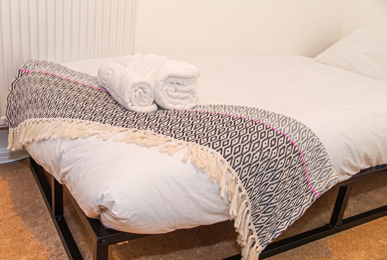 Una cama con un edredón estampado, toallas enrolladas y una almohada lisa.