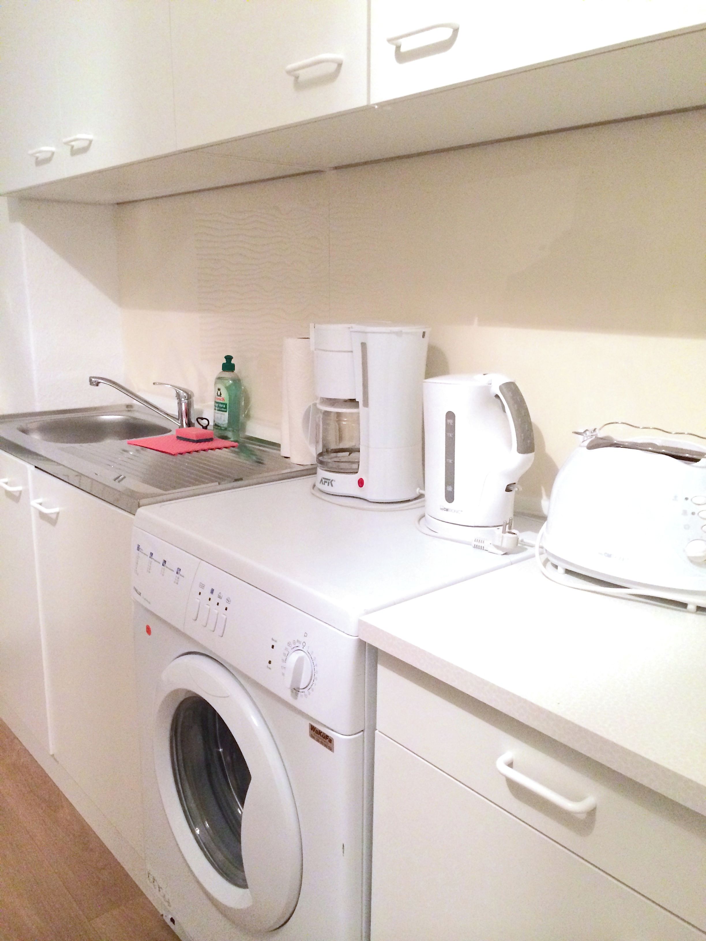 A compact kitchen with a washing machine, a coffee maker, and a toaster on the countertop.