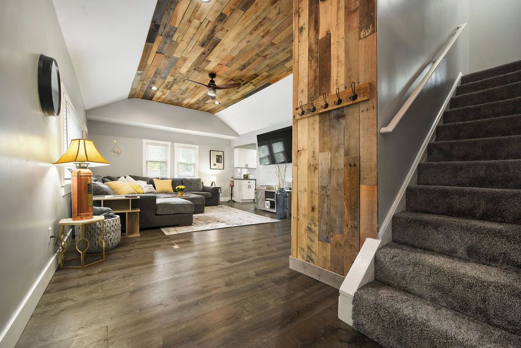 A spacious living area with a high ceiling, a staircase, and a kitchen in the background.