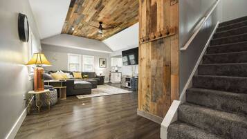 A spacious living area with a high ceiling, a staircase, and a kitchen in the background.