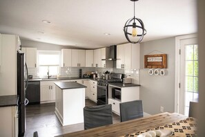 Une cuisine moderne avec des meubles blancs, un îlot central et un coin repas comprenant une table et des chaises en bois.