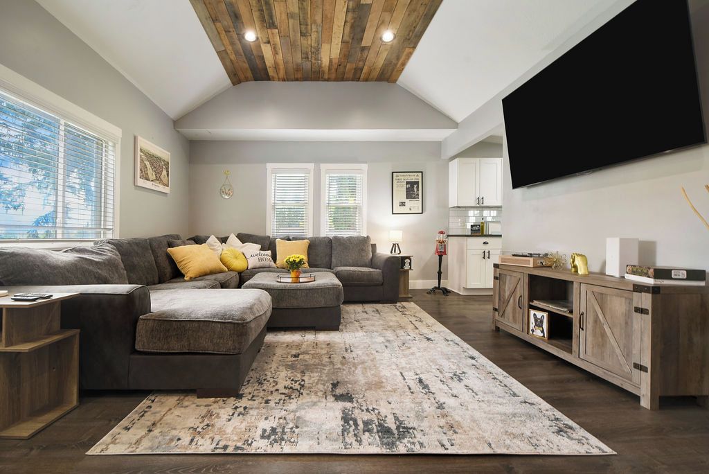 A modern living room with a sectional sofa, a coffee table, and a TV. There is a kitchen in the background.
