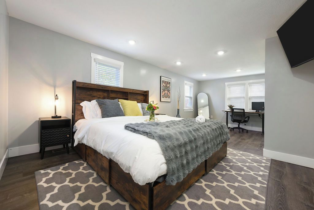 A bedroom with a bed, bedside table, lamp, and a desk with a chair.