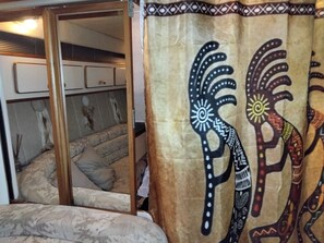 Une chambre avec un lit, un miroir et un rideau orné de motifs tribaux.